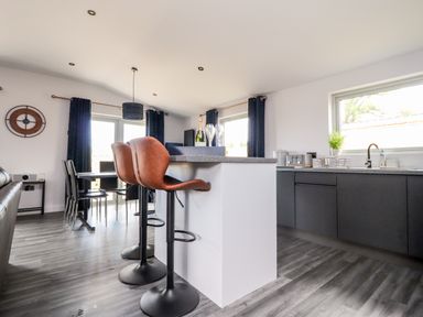 A kitchen and dining area with bar stools and a clock on the wall at Box Tree Escapes Wennington near Kirkby Lonsdale