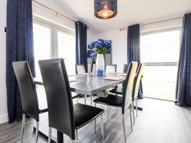 A dining room with a black table and black chairs a vase with flowers and dark curtains at Box Tree Escapes Wennington near Kirkby Lonsdale
