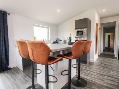 A kitchen with a countertop and four brown bar stools near a microwave at Box Tree Escapes in Wennington near Kirkby Lonsdale