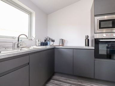 A kitchen with dark grey cabinets a sink under a window and built in oven and microwave at Box Tree Escapes in Wennington near Kirkby Lonsdale