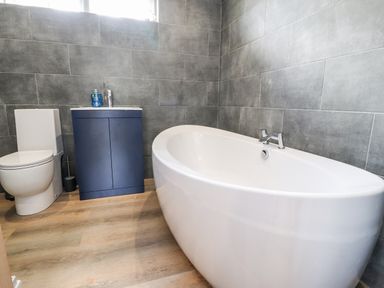 A bathroom with a white bathtub a toilet and a blue cabinet with a sink at Box Tree Escapes Wennington near Kirkby Lonsdale