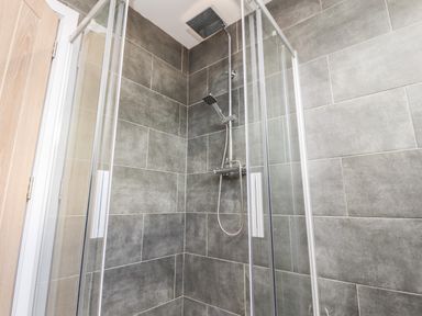 A corner shower enclosure with glass doors and a rainfall showerhead in a bathroom with gray tiled walls at Box Tree Escapes in Wennington near Kirkby Lonsdale