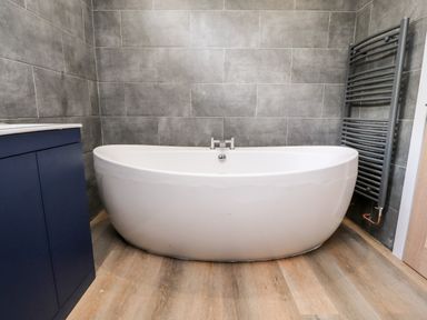 A bathroom with a white bathtub dark tiled walls wooden floor and a dark towel radiator at Box Tree Escapes Wennington near Kirkby Lonsdale