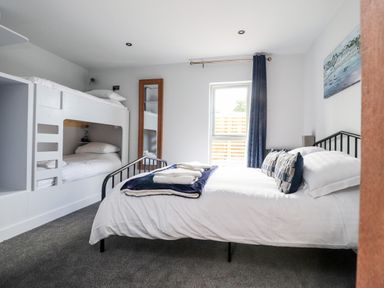 A bedroom with a double bed and bunk beds a full-length mirror and a window with dark curtains at Box Tree Escapes Wennington near Kirkby Lonsdale