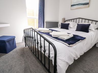 A bedroom with a bed with black metal frame a window with blue curtains and folded towels on the bed at Box Tree Escapes Wennington near Kirkby Lonsdale
