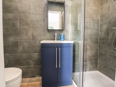 A bathroom with a blue vanity cabinet a mirror a partially visible toilet and a shower enclosure at Box Tree Escapes in Wennington near Kirkby Lonsdale