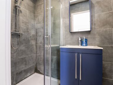 A bathroom with a shower enclosure and a blue sink cabinet with a mirror at Box Tree Escapes in Wennington near Kirkby Lonsdale