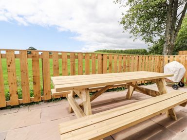 A wooden picnic table and bench on a stone patio with a wooden fence and green fields in the background at Box Tree Escapes in Wennington near Kirkby Lonsdale