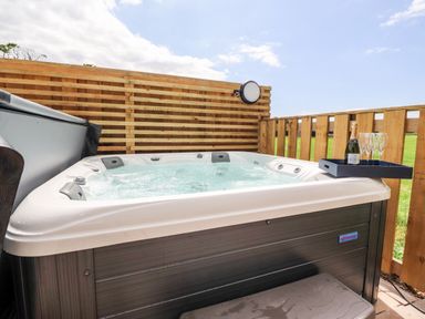 An outdoor hot tub with a bottle and glasses on a tray on the edge at Box Tree Escapes Wennington near Kirkby Lonsdale
