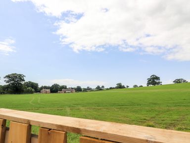 A green field with a few houses in the distance under a partly cloudy sky at Box Tree Escapes in Wennington near Kirkby Lonsdale