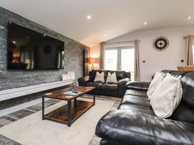 A living room with two black leather sofas a wooden coffee table and a wall mounted television at Box Tree Escapes in Wennington near Kirkby Lonsdale