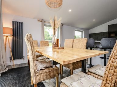 A dining area with a wooden table and woven chairs with cushions and a vase with dried plants on the table at Box Tree Escapes in Wennington near Kirkby Lonsdale