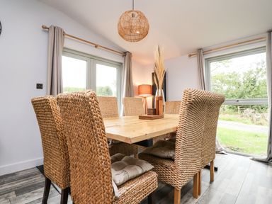 A dining room with wicker chairs and a wooden table by windows at Box Tree Escapes Wennington near Kirkby Lonsdale
