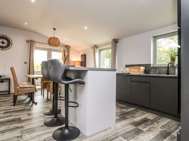 A kitchen with a breakfast bar and stools dining table and chairs and windows at Box Tree Escapes in Wennington near Kirkby Lonsdale