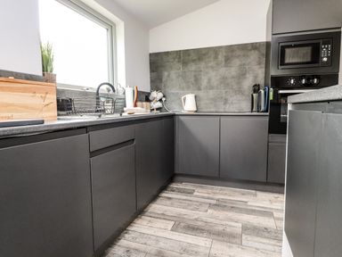 A kitchen with grey cabinets a window a white kettle a microwave and wooden flooring at Box Tree Escapes Wennington near Kirkby Lonsdale