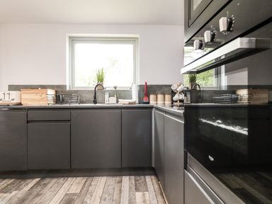 A kitchen with dark grey cabinets wooden floor and a window above the sink at Box Tree Escapes in Wennington near Kirkby Lonsdale