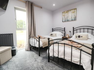 A bedroom with two single beds a window with curtains and a bedside table at Box Tree Escapes Wennington near Kirkby Lonsdale