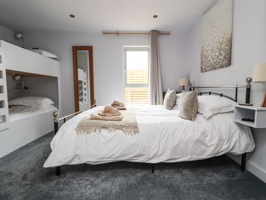 A bedroom with a double bed towels on bed bunk beds a window a tall mirror and bedside lamps at Box Tree Escapes Wennington near Kirkby Lonsdale