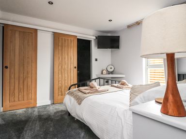 A bedroom with a bed carpet wooden sliding doors a wall mounted tv and a lamp at Box Tree Escapes in Wennington near Kirkby Lonsdale