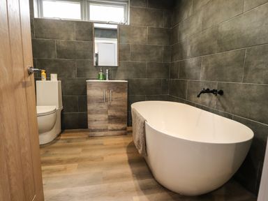 A bathroom with a white bathtub a wooden vanity with a mirror above and a toilet at Box Tree Escapes Wennington near Kirkby Lonsdale