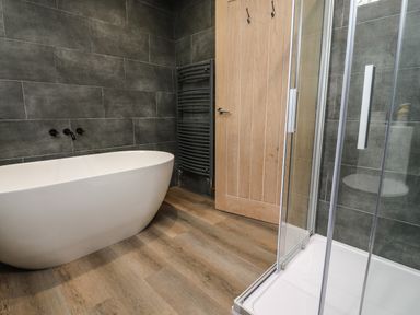 A bathroom with a freestanding bathtub a glass shower enclosure a wooden door and a black towel radiator at Box Tree Escapes Wennington near Kirkby Lonsdale