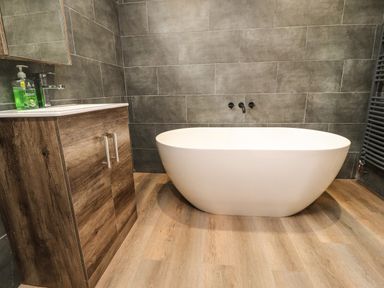 A bathroom with a freestanding white bathtub wooden vanity with sink and dark gray tiled walls at Box Tree Escapes in Wennington near Kirkby Lonsdale