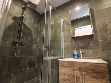A bathroom with a glass shower enclosure a showerhead a wooden cabinet with a sink and a mirror at Box Tree Escapes in Wennington near Kirkby Lonsdale