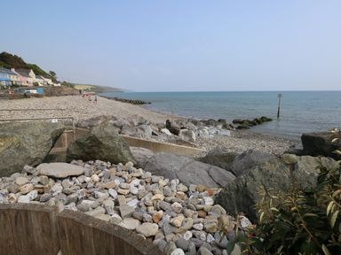 A rocky beach with pebbles and large rocks by the sea and houses along the shore at Oakland Cottage in Summerhill near Saundersfoot