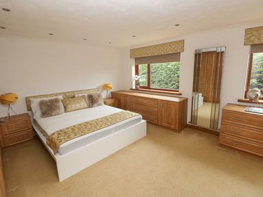 A bedroom with a bed, two bedside tables with lamps, a large wooden dresser, a wall mirror and two windows at Oakland Cottage in Summerhill near Saundersfoot