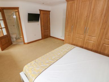 A bedroom with a bed yellow patterned runner wooden wardrobe two wooden doors a wall mounted tv and an en suite bathroom at Oakland Cottage in Summerhill near Saundersfoot