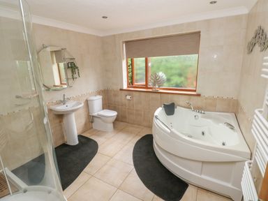 A bathroom with a corner bathtub a toilet a sink a shower and a window with a blind at Oakland Cottage Summerhill near Saundersfoot