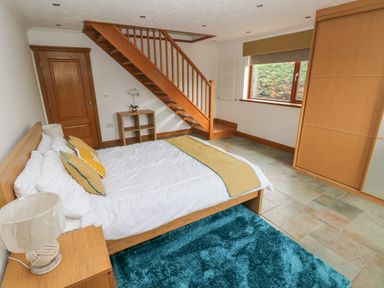 A bedroom with a bed pillows a lamp a rug a wooden staircase a window and a wardrobe at Oakland Cottage in Summerhill near Saundersfoot