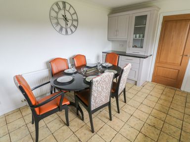 A dining room with a black oval table six chairs and a large wall clock at Oakland Cottage Summerhill near Saundersfoot