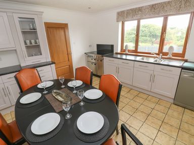 A kitchen with a round dining table set with plates and glasses next to cabinets and a window at Oakland Cottage in Summerhill near Saundersfoot
