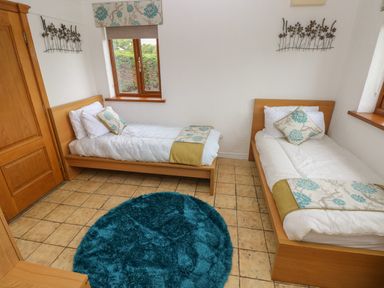 A bedroom with two single beds wooden furniture and a round blue rug at Oakland Cottage in Summerhill near Saundersfoot