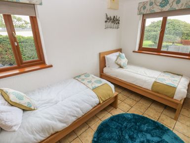 A bedroom with two single beds a blue round rug and windows showing outdoor greenery at Oakland Cottage in Summerhill near Saundersfoot