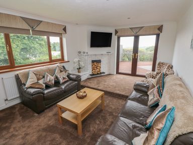 A living room with brown leather sofas a coffee table a white brick fireplace and large windows at Oakland Cottage in Summerhill near Saundersfoot