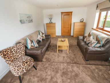 A living room with two brown sofas a leopard print chair a wooden coffee table and two wooden dressers at Oakland Cottage in Summerhill near Saundersfoot