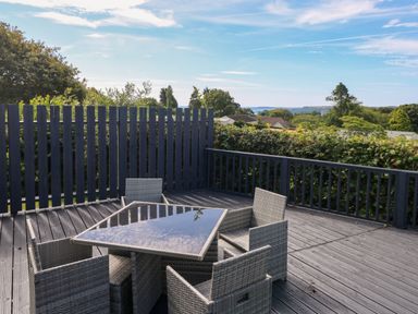 An outdoor deck with a glass top table and four wicker chairs surrounded by a railing and greenery at Oakland Cottage in Summerhill near Saundersfoot