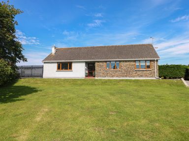 A single-story house with a mixed stone and white exterior and a large grassy lawn at Oakland Cottage in Summerhill near Saundersfoot