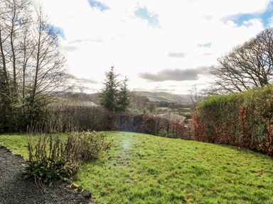 A garden with grass shrubs and trees with hills in the background at Valley View in Rhayader