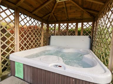 A hot tub with water inside a wooden gazebo with lattice walls at Valley View in Rhayader