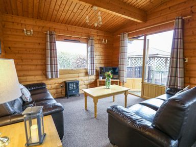 A living room with two leather sofas a wooden coffee table with flowers a TV and windows with curtains at Valley View in Rhayader