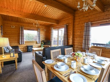 A wooden cabin interior with a dining table set and leather sofas at Valley View in Rhayader