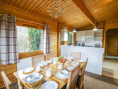 A dining area with a set table next to a kitchen in a wooden cabin at Valley View in Rhayader