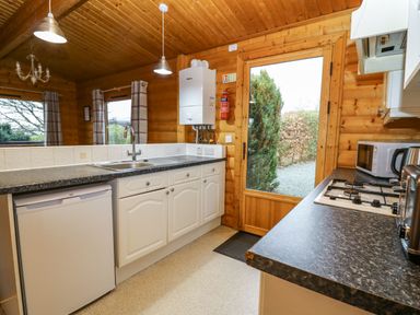A kitchen with white cabinets a sink a stove a microwave and a glass door showing an outdoor view at Valley View in Rhayader