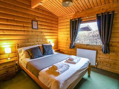A bedroom with a double bed two bedside tables and lamps wooden walls and ceiling a window with dark curtains and folded towels on the bed at Valley View in Rhayader