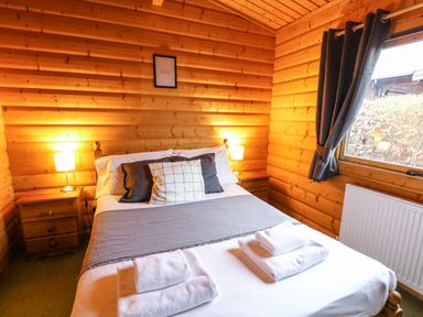 A bedroom with a double bed bedside tables and lamps in a wooden cabin at Valley View in Rhayader