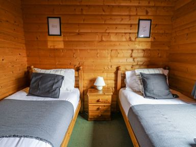 A bedroom with two single beds a wooden nightstand with a lamp and framed pictures on the wall at Valley View in Rhayader