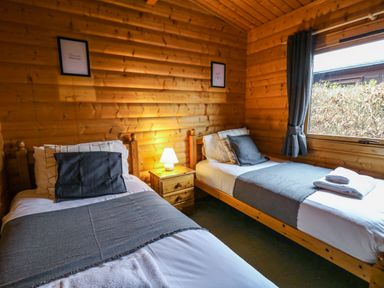 A bedroom with two single beds a wooden nightstand with a lamp and a window with curtains at Valley View in Rhayader